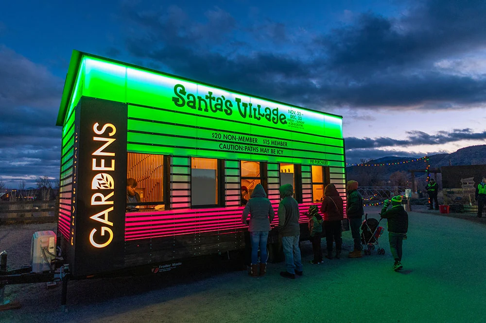Trailer Made Santa’s Village ticket booth at Chatfield Farms with illuminated green and pink branding and guests at the service windows